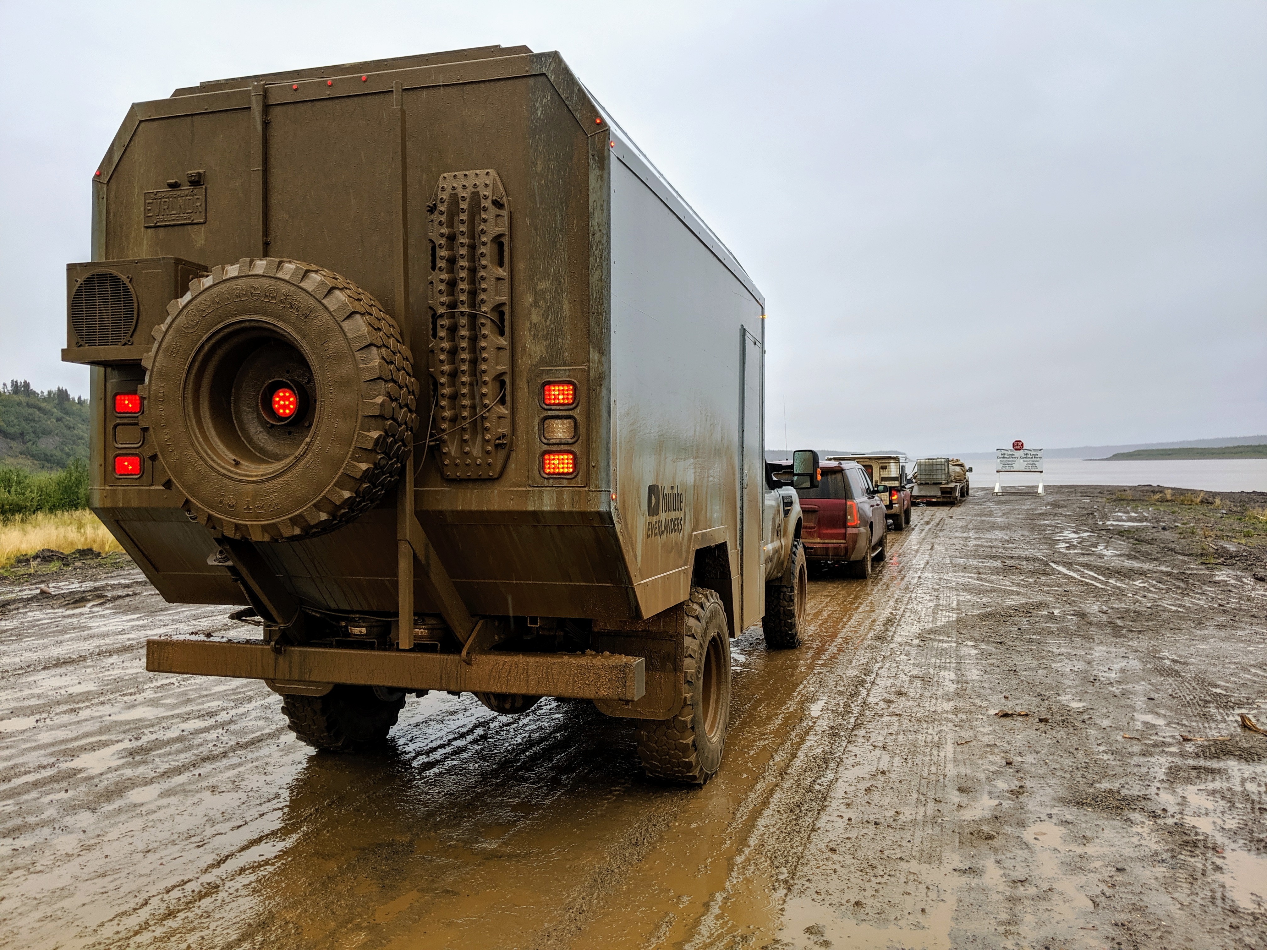 A row of off-road vehicles parked on a muddy road near the Arctic Ocean, with a sign visible in the distance.