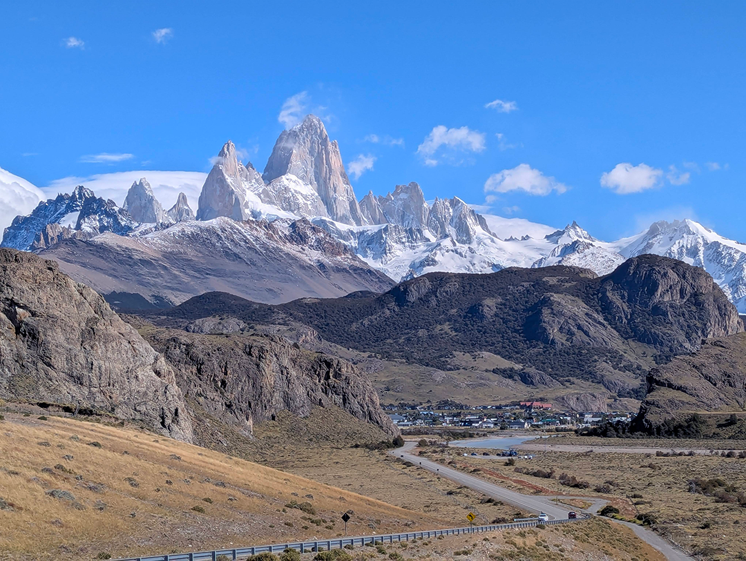 Panoramic view of the snow-capped peaks of Patagonia with a clear blue sky and winding road in the foreground.