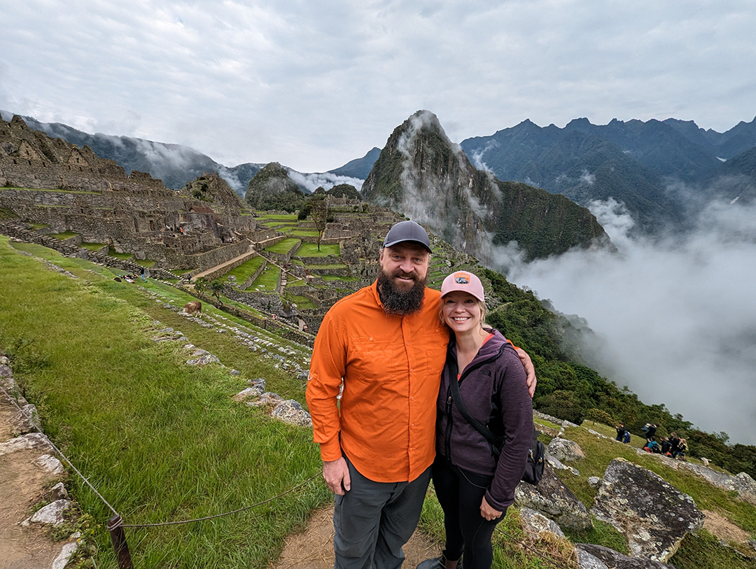 Jason and Kara together at Machu Picchu, surrounded by lush greenery and mountains, with mist in the background.
