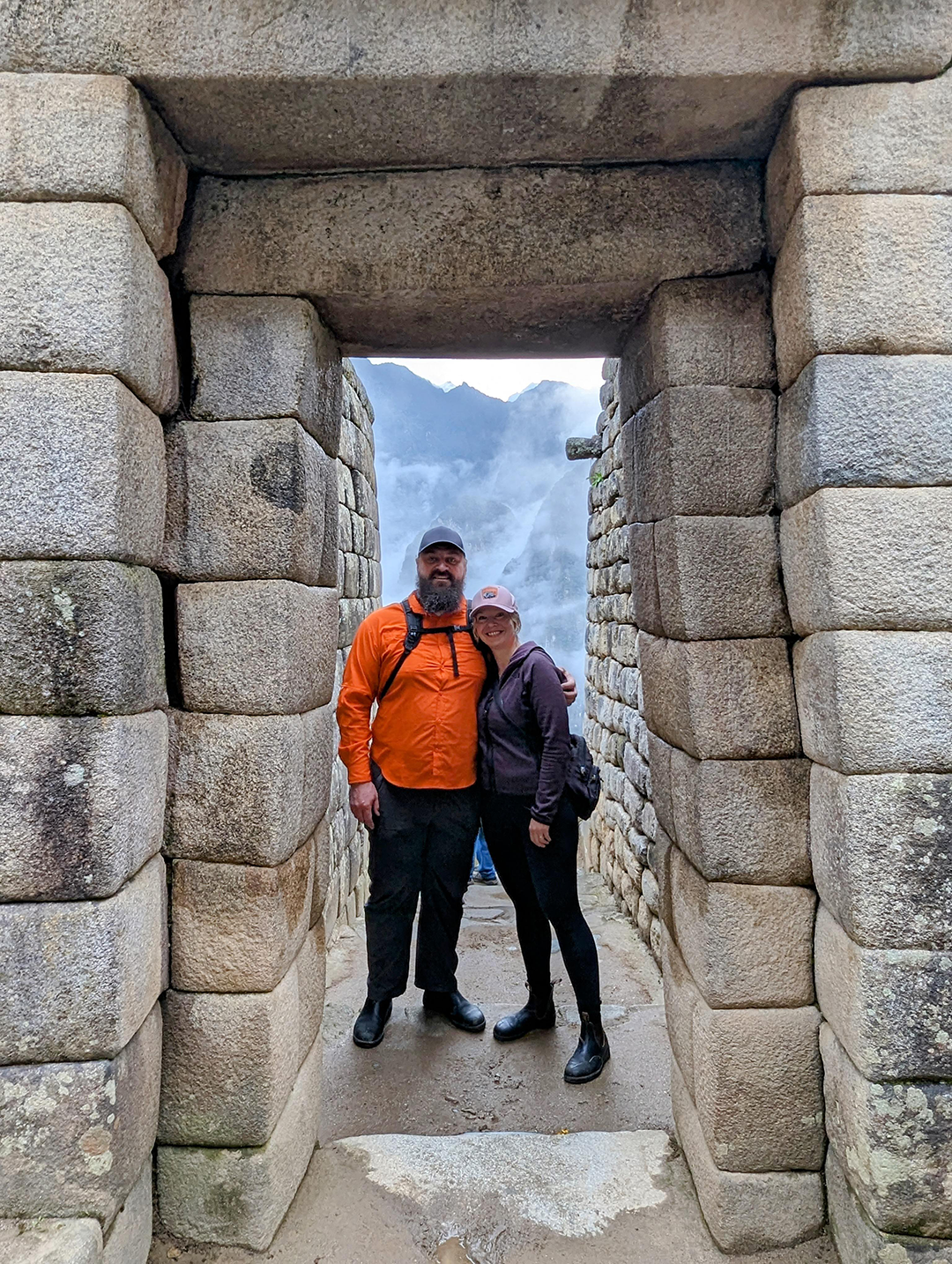 Jason and Kara in a stone archway at Machu Picchu, surrounded by misty mountains.
